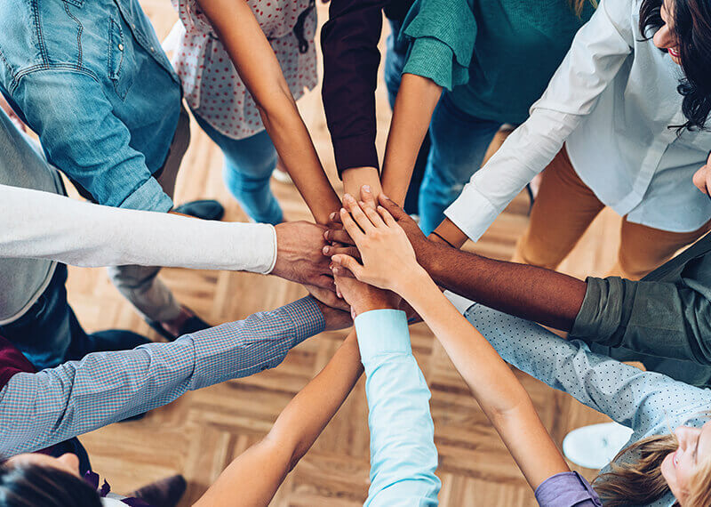 Men and Women of all races putting their hands on top of each other in a circle