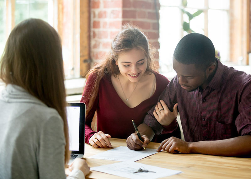 A couple signing paperwork in an office with another woman looking on