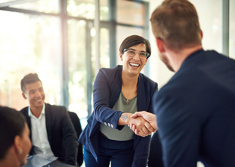 A man and woman shaking hands smiling in an office