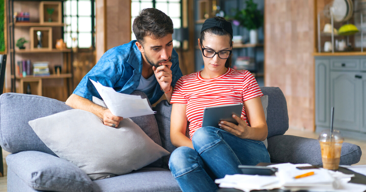 Young couple working on computer while calculating finances sitting on couch