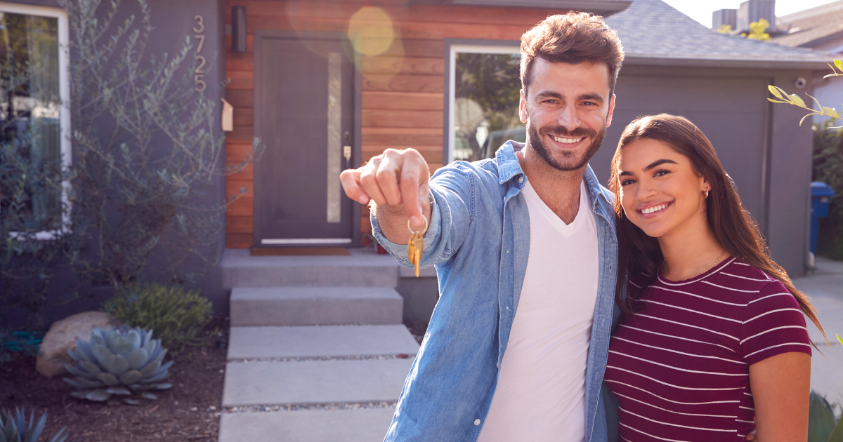 Portrait Of Couple Standing Outdoors In Front Of House Holding Keys