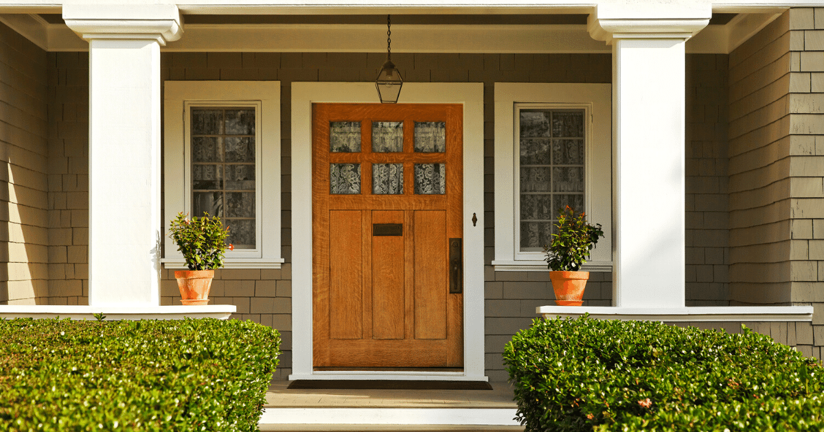 A concrete walkway bordered with hedged shrubs leads to the front door of a home. 