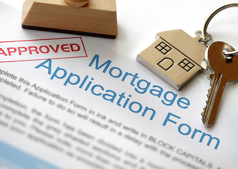 A mortgage application form with the red approved stamped in red and a key with a house keychain in silver