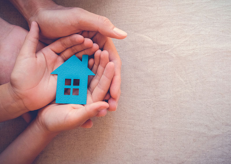 An adult holding the hands of a child who is holding a blue paper house