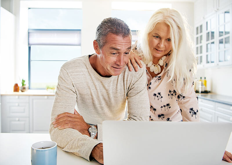 An eldery couple looking at a computer screen in their kitchen