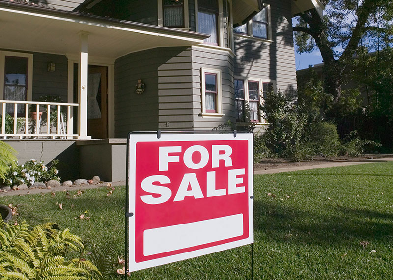 A red and white for sale sign sitting on the lawn in front of a house