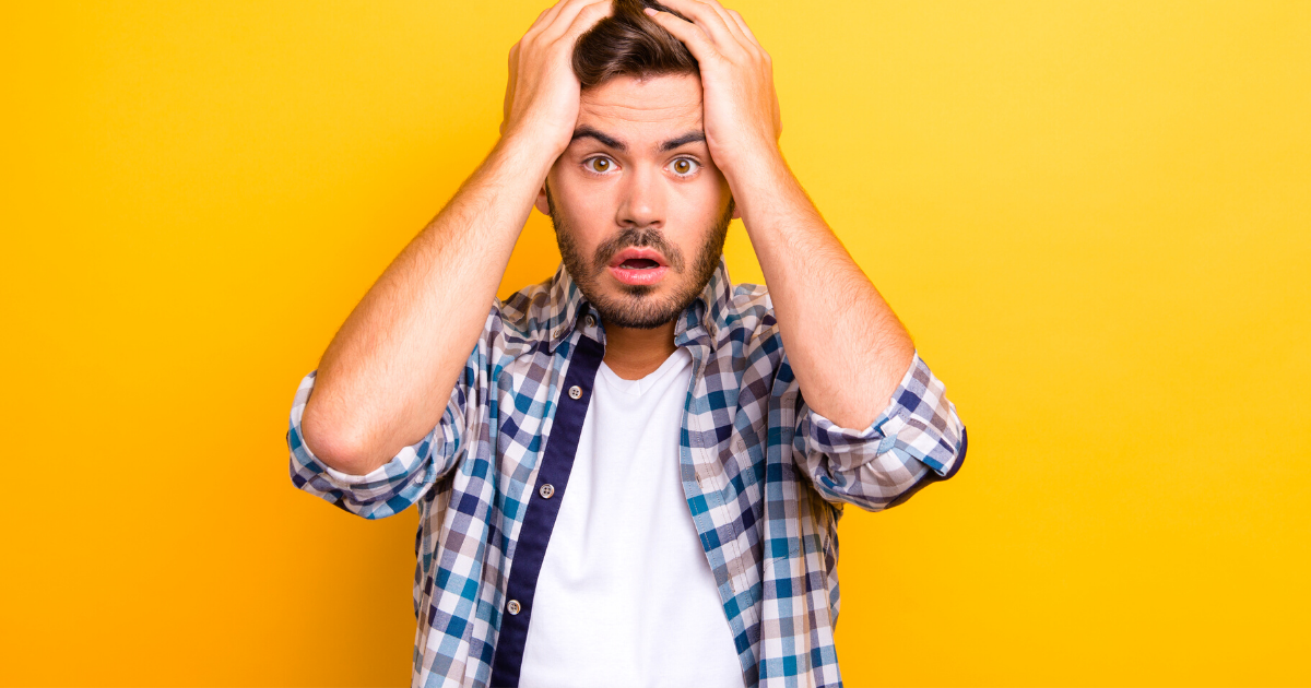 Portrait of frightened brunette man in a plaid shirt holds his hands behind his head and looks into the camera isolated on shine yellow background