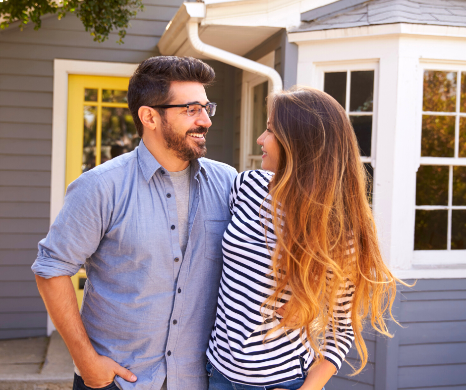 Portrait Of Excited Couple Standing Outside New Home