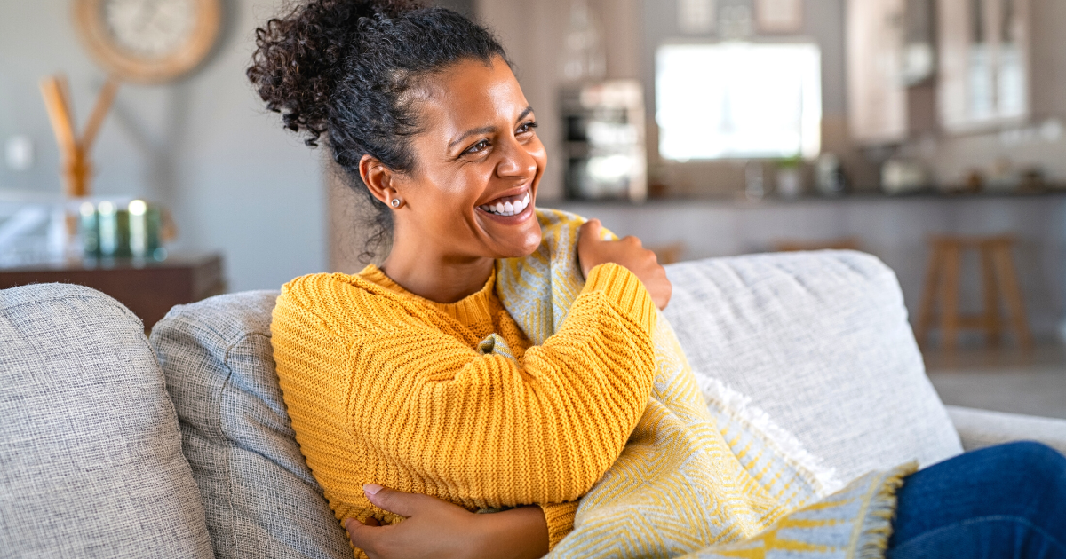 Joyful woman with blanket on couch laughing