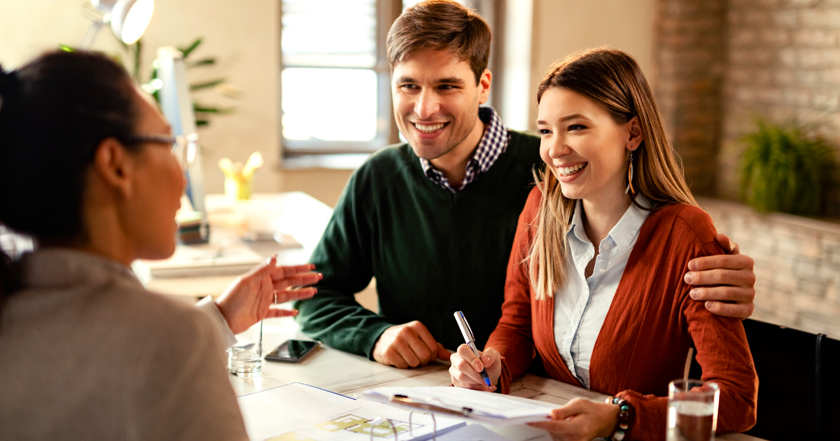 Happy couple signing mortgage contract while having meeting with real estate agent