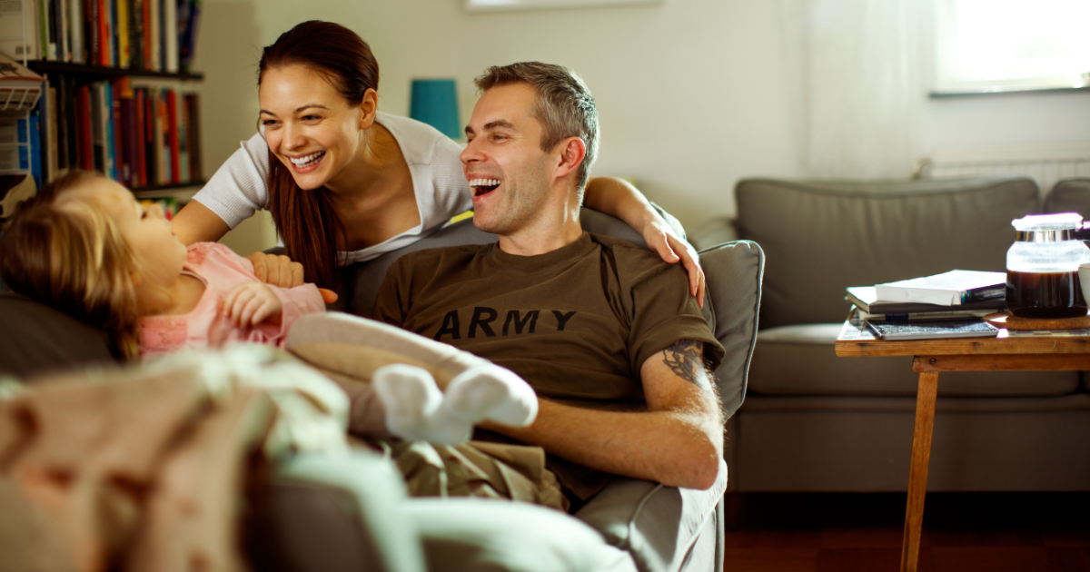 Army father and his wife playing with their child on the couch