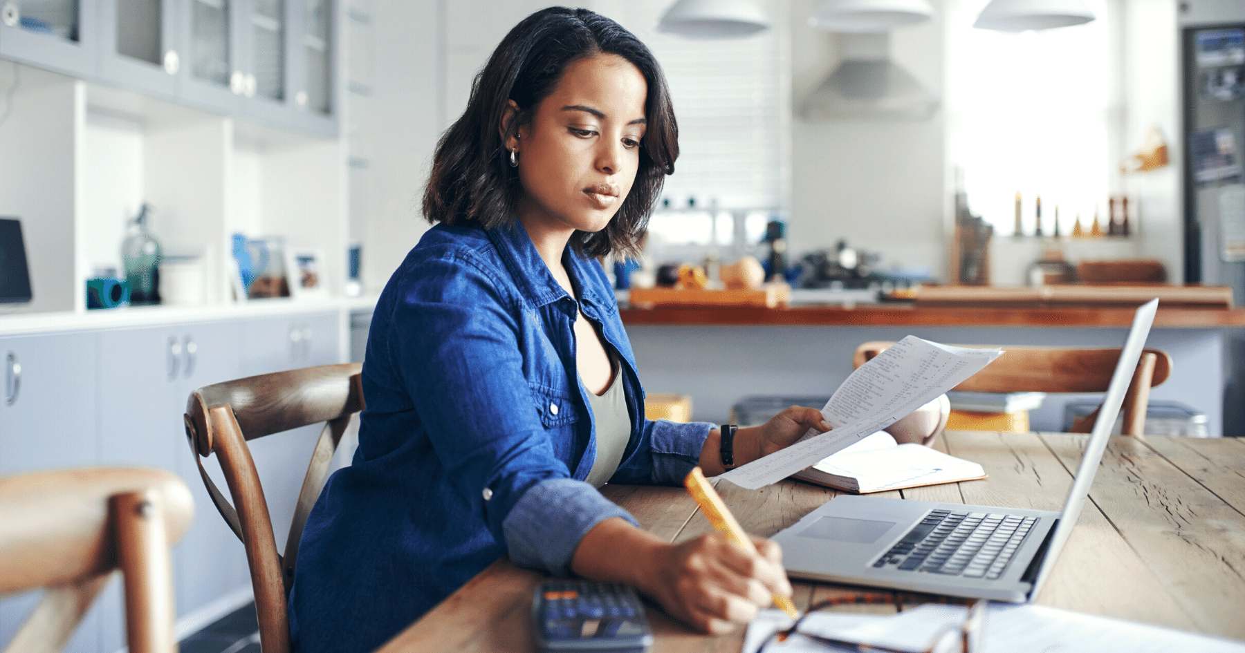 Shot of a young woman using a laptop and going through paperwork while working from home