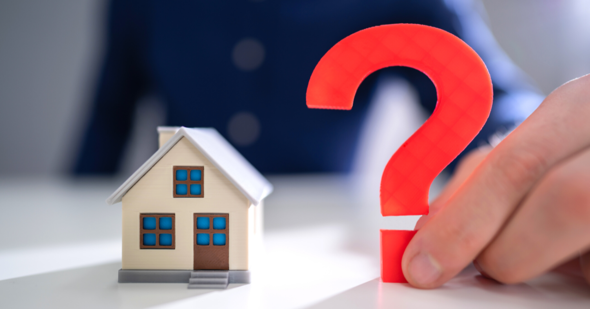 Man Holding Red Question Mark Next To Wooden House Model