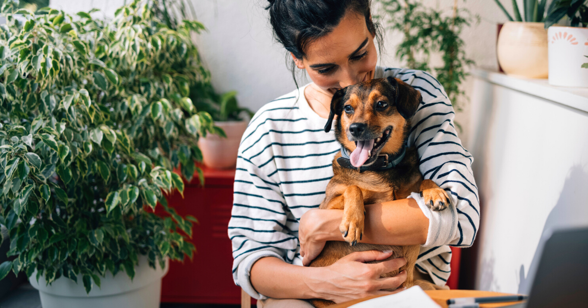 Woman holding her dog in her house surrounded by houseplants