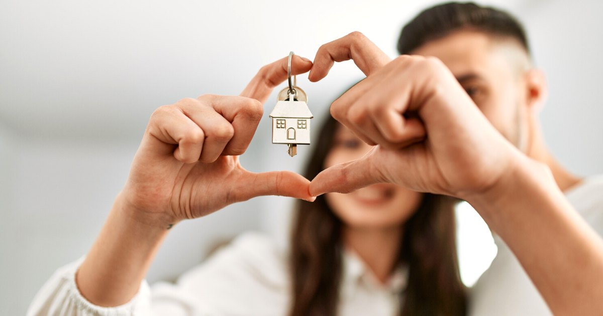 Young couple doing heart symbol with fingers and holding key of new home