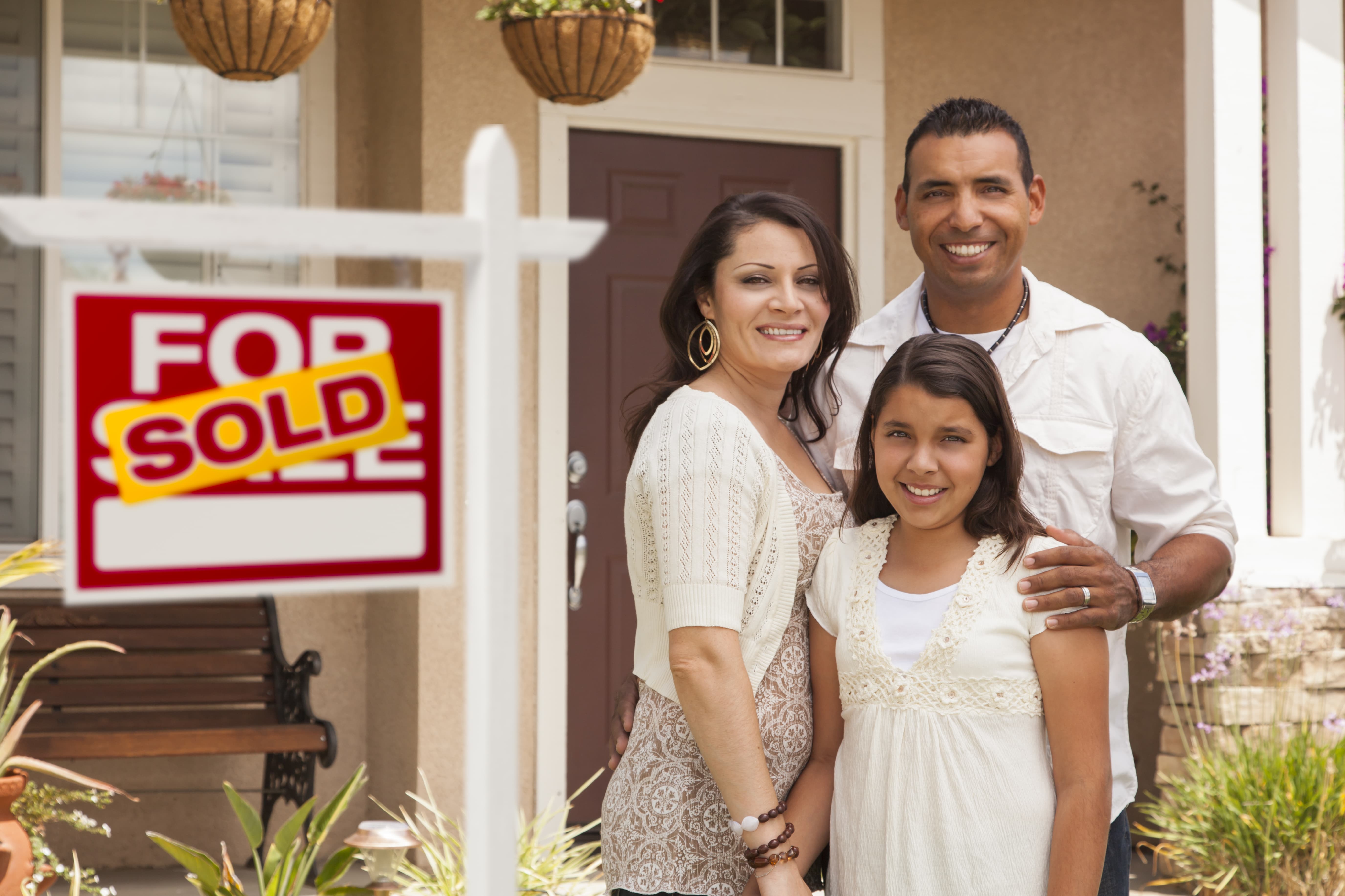 A family of three standing in front of a house with a sold sign