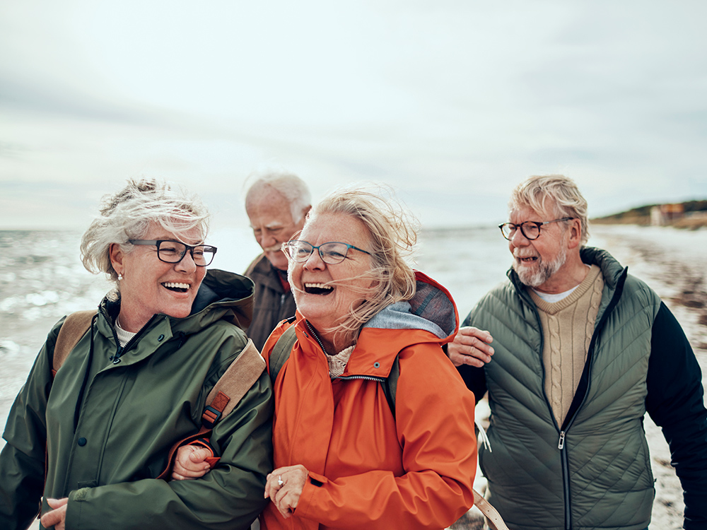 Two older couples walking on the beach laughing